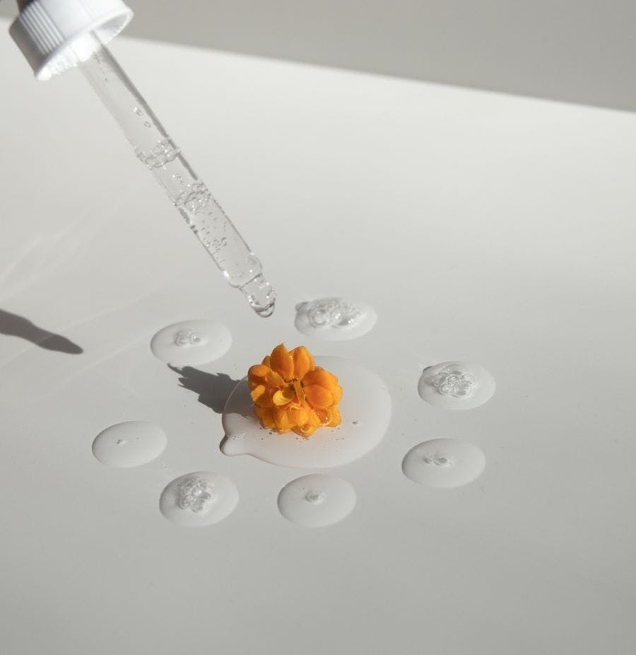 Image d'une pipette d'huile essentielle qui verse une goutte sur une fleur